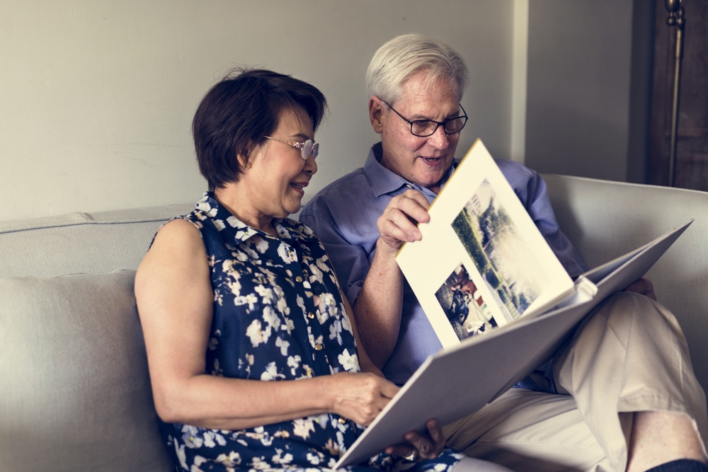 A senior couple sit on the couch and look at photos together
