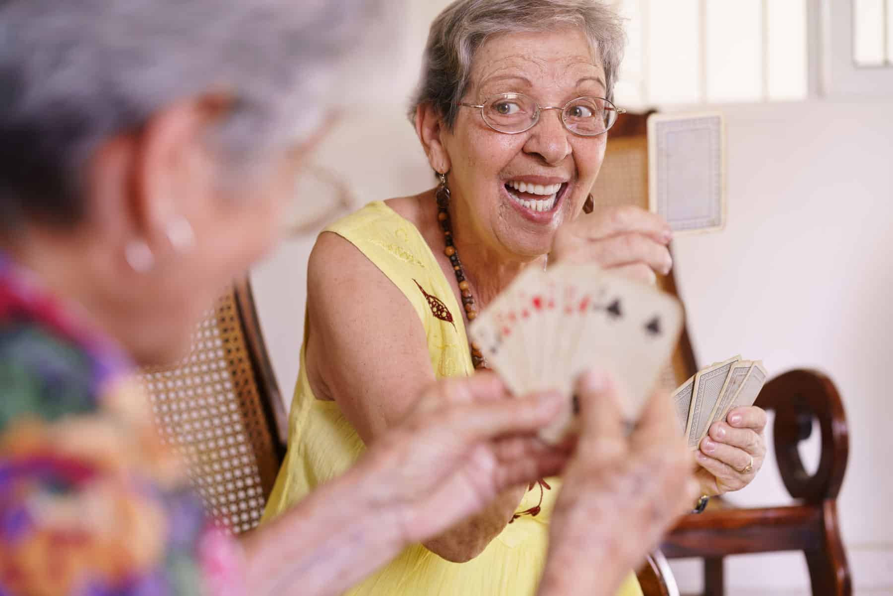 Two senior women laugh as they play cards together