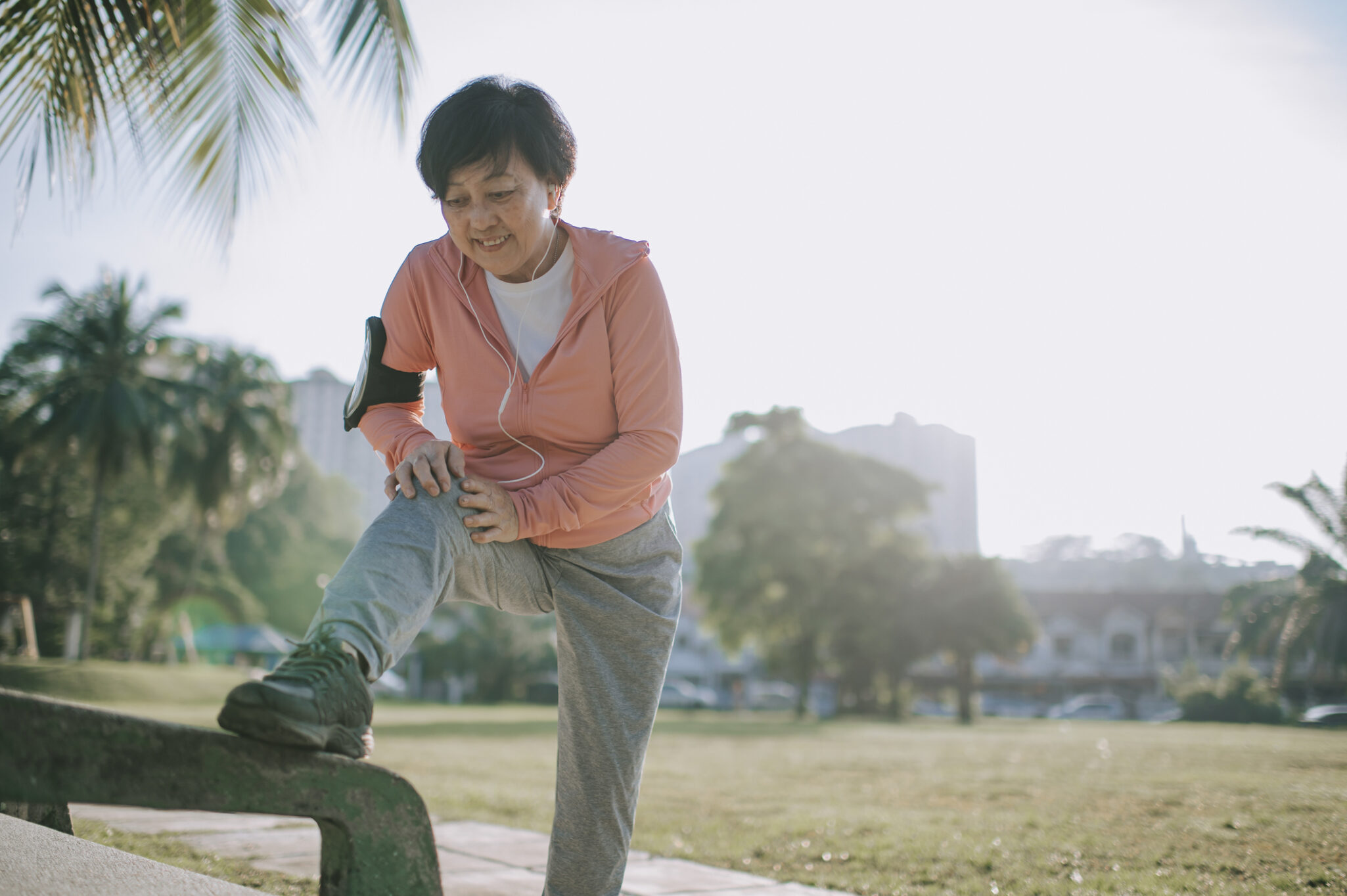 A senior woman places her foot up on a park bench to stretch out before exercising