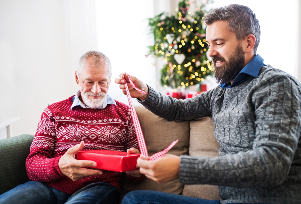 Senior man opens gift with adult son.