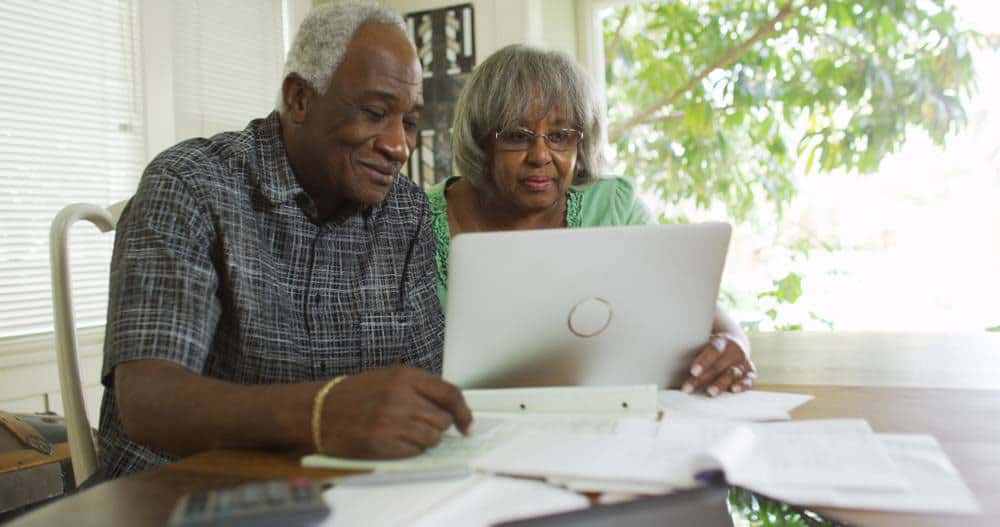 Two African American elders using computer with bills