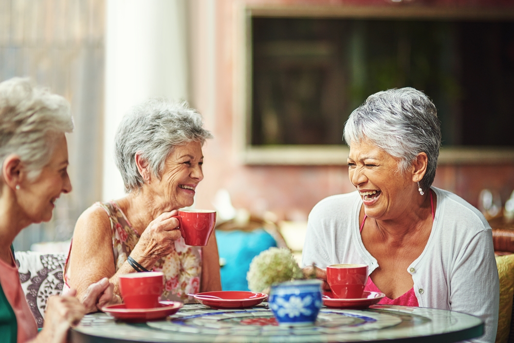 a group of female seniors laugh together while drinking coffee