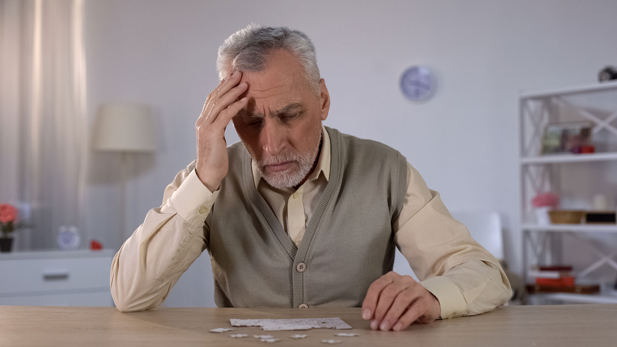 a senior man places hand on head while completing a puzzle